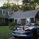 Rear-quarter view of Miles Bron's Porsche 918 Spyder parked in a driveway from Glass Onion: A Knives Out Story